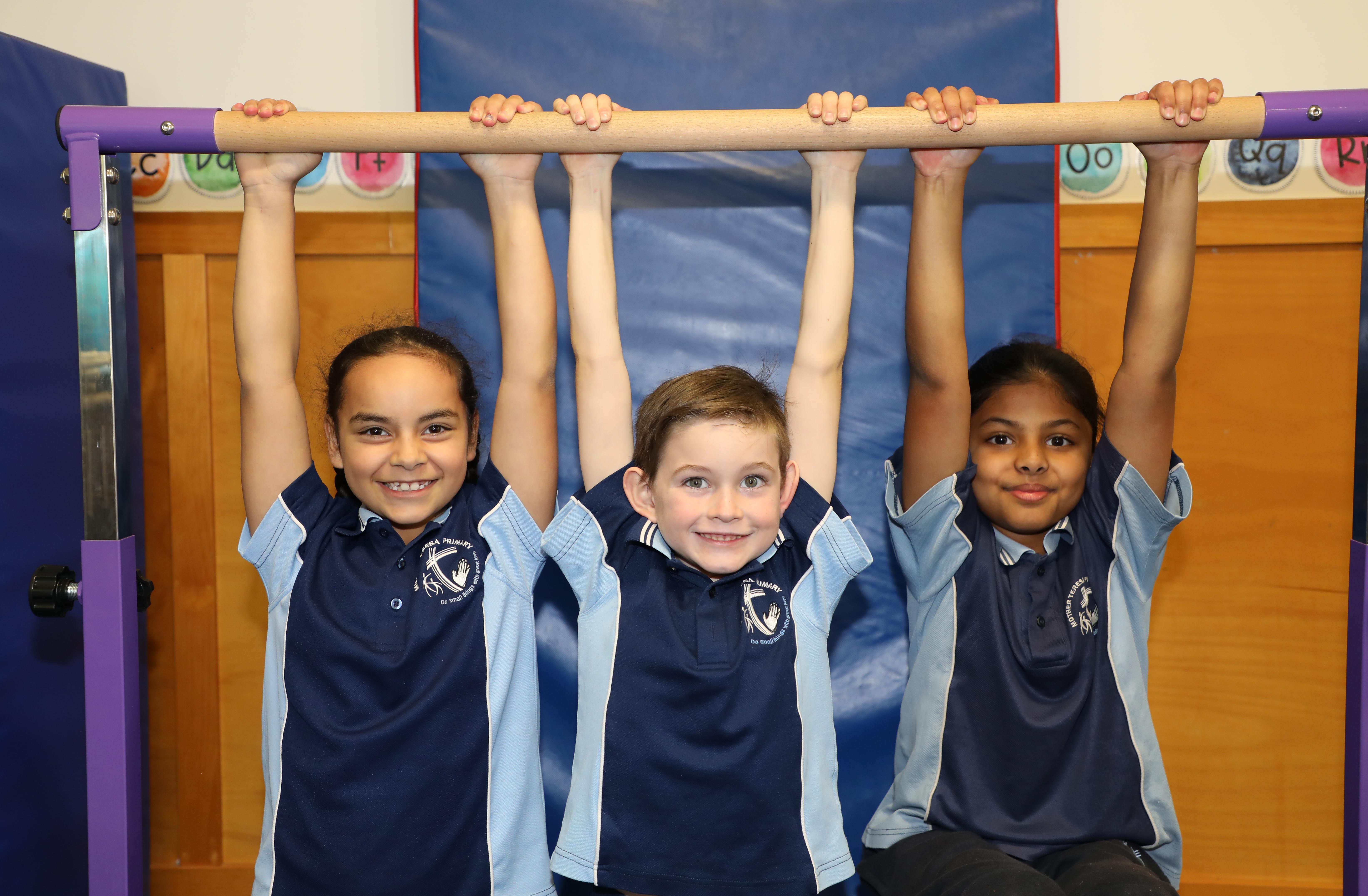 Students in school uniforms hanging from a gymnastics bar indoors.