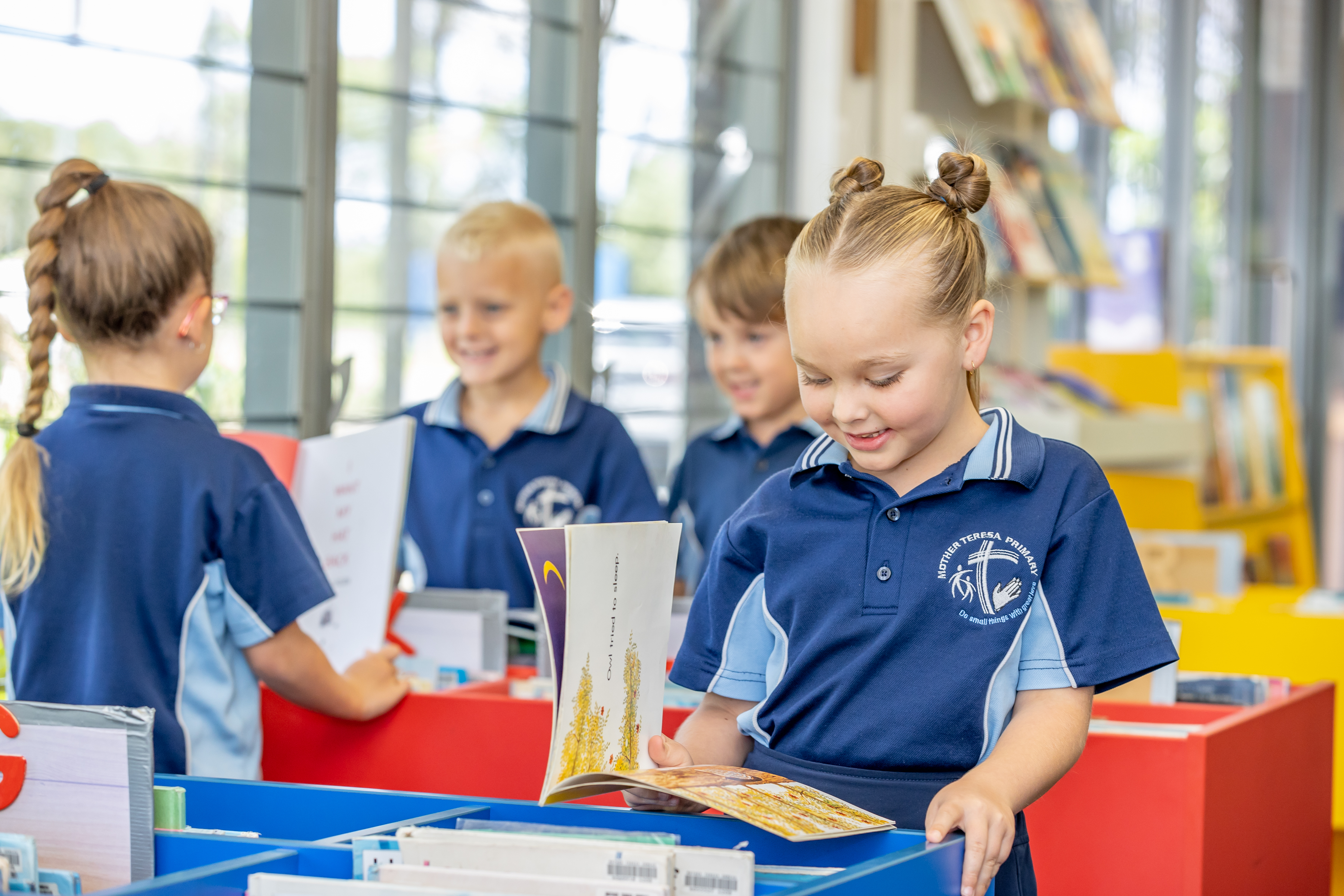 Students in school uniforms browsing and reading books in a classroom library area.