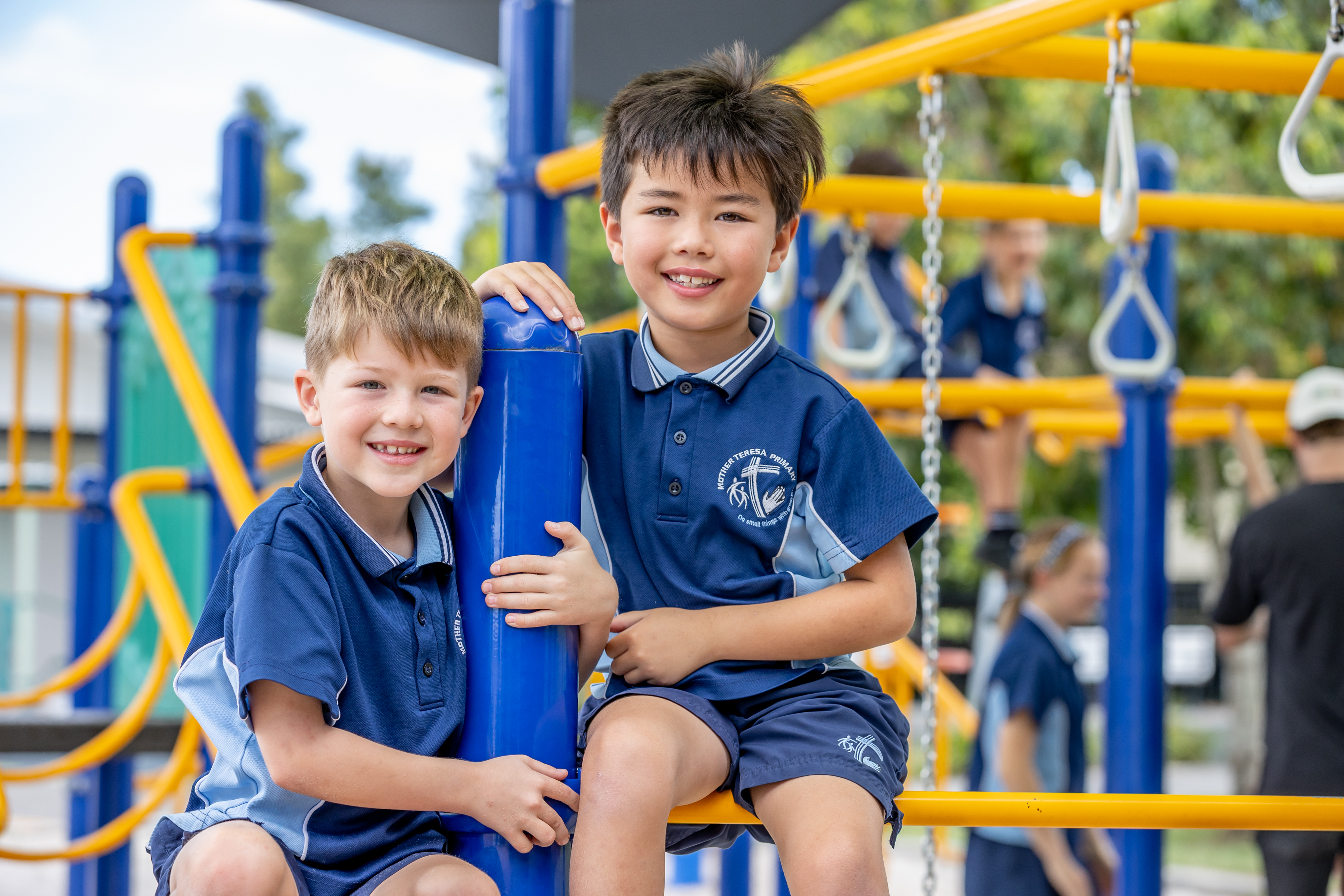 Two students sitting on playground equipment with climbing structures behind them.