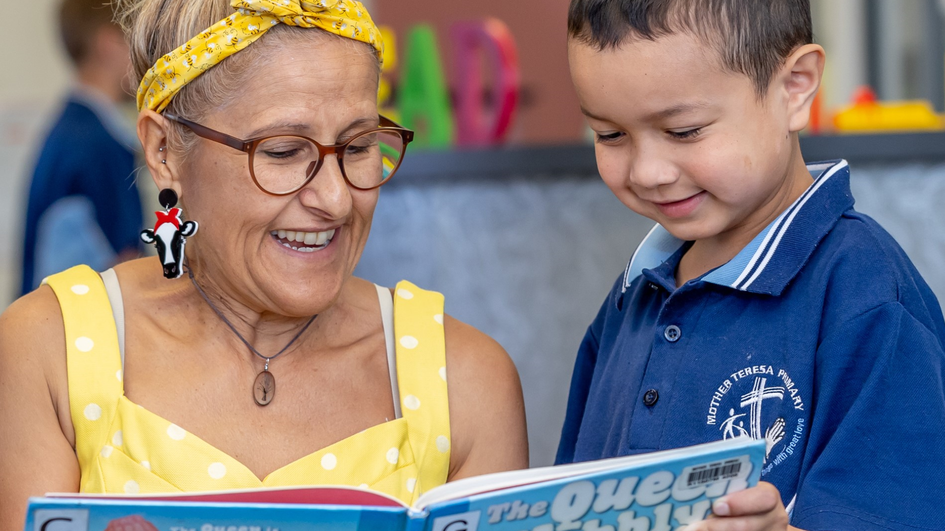 Adult and student reading a book together in a classroom setting.
